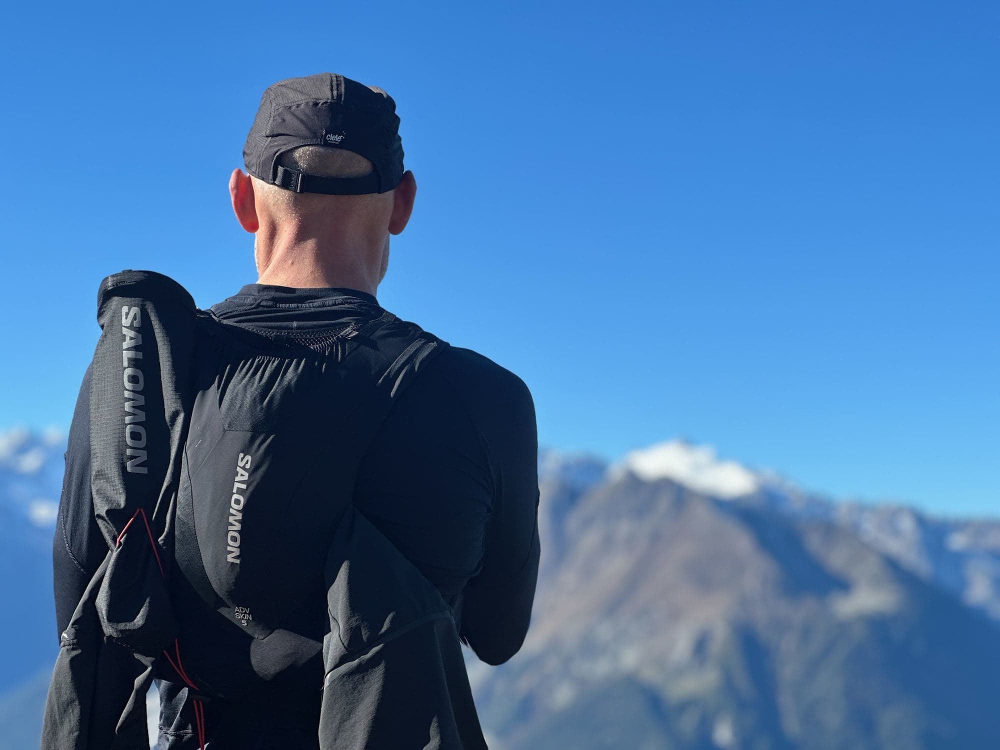 Trail runner con lo zaino da gara che guarda montagne innevate
