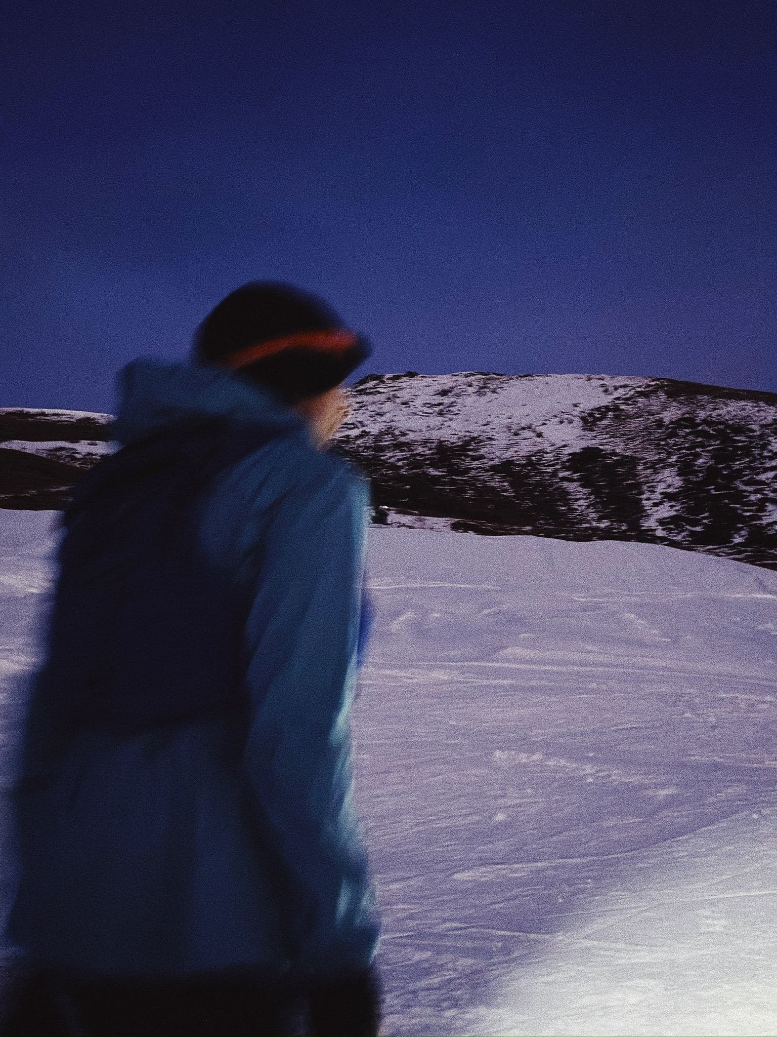Corsa invernale con giacca e frontale attraverso un nevaio al tramonto